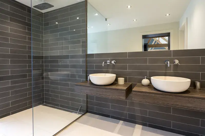 Remodeled bathroom with gray tile walls, rain shower and double bowl vanity