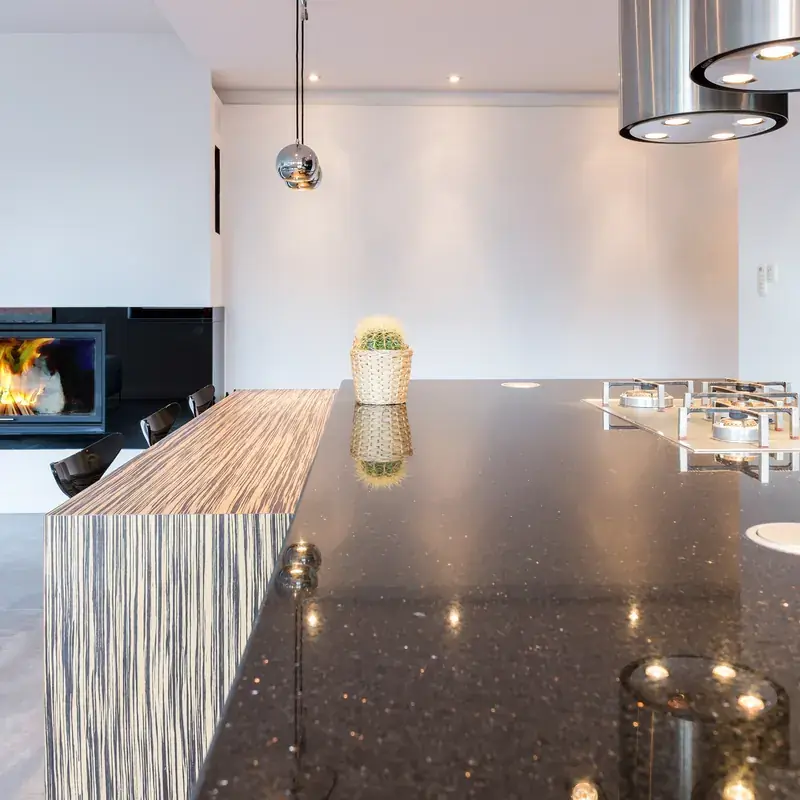 Open kitchen with black quartz countertops, chrome range hood and fireplace